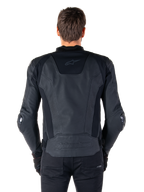 Alpinestars Missile V3 Leren Jas, achteraanzicht van een motorrijder, zwart, premium lederen constructie met technische stretchpanelen, Alpinestars-logo in reliëf op de onderrug en subtiele branding op de bovenrug, gecombineerd met zwarte broek voor een gecoördineerde racing sport-look