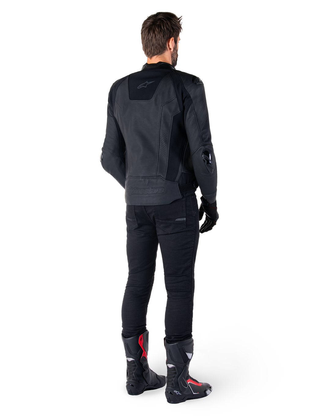 Alpinestars Missile V3 Leren Jas in het zwart, achteraanzicht op een rijder, gedragen met zwarte broek en zwart-rode racelaarzen, voorzien van een gestroomlijnde leren constructie met subtiele branding en een sportieve racepasvorm
