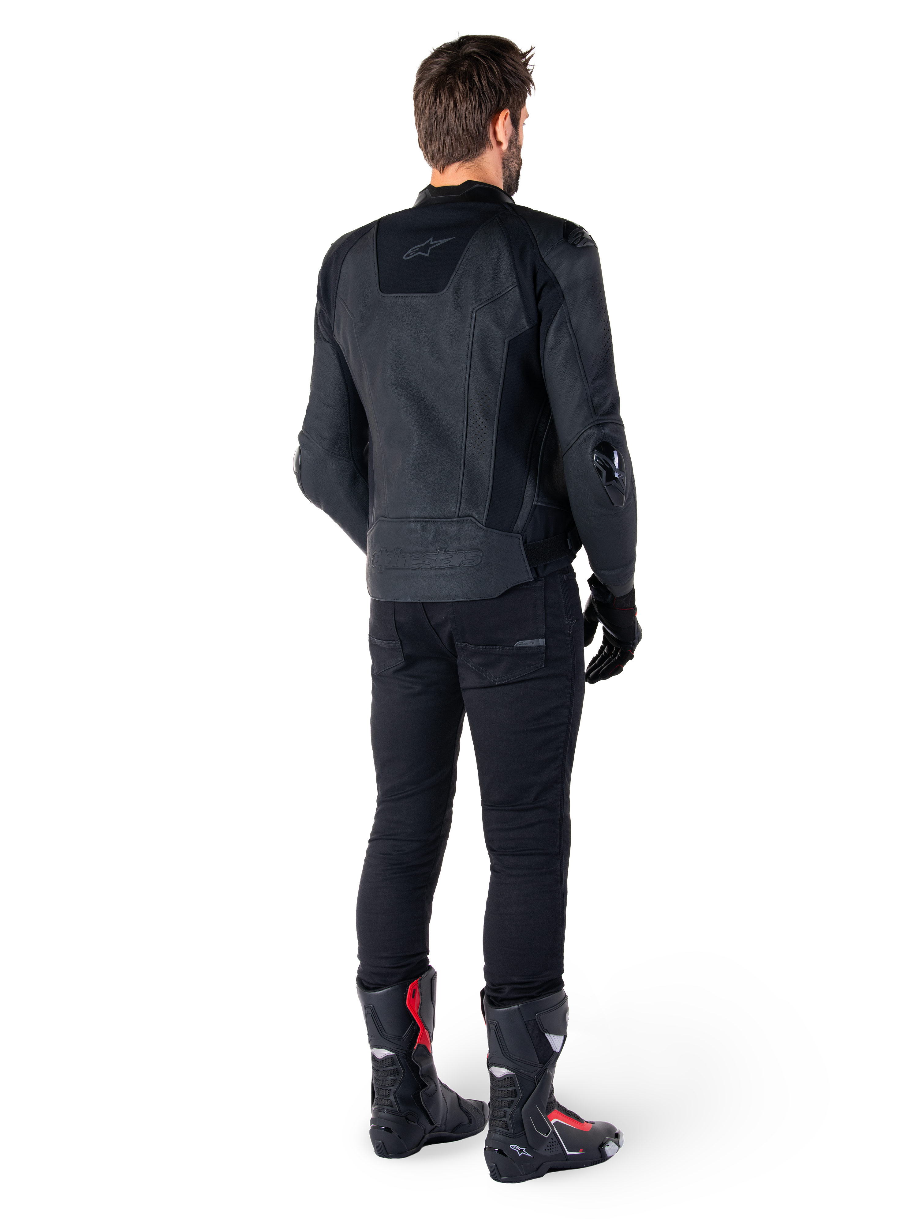 Alpinestars Missile V3 Leren Jas in het zwart, achteraanzicht op een rijder, gedragen met zwarte broek en zwart-rode racelaarzen, voorzien van een gestroomlijnde leren constructie met subtiele branding en een sportieve racepasvorm
