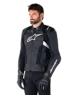Alpinestars Missile V3 leren jas, zwart en wit, gedragen door een man met zwarte motorhandschoenen, voorzien van een opvallend wit Alpinestars-logo op de borst, externe schoudersliders en geperforeerde panelen voor een racing-geïnspireerde look