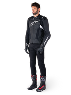 Mannelijke motorrijder die de Alpinestars Missile V3 lederen jas in het zwart en wit draagt, voorzien van een wit logo op de borst en geperforeerde lederen panelen, gecombineerd met een zwarte motorbroek, zwarte handschoenen en zwart-rode racelaarzen voor een complete sportieve motoroutfit.