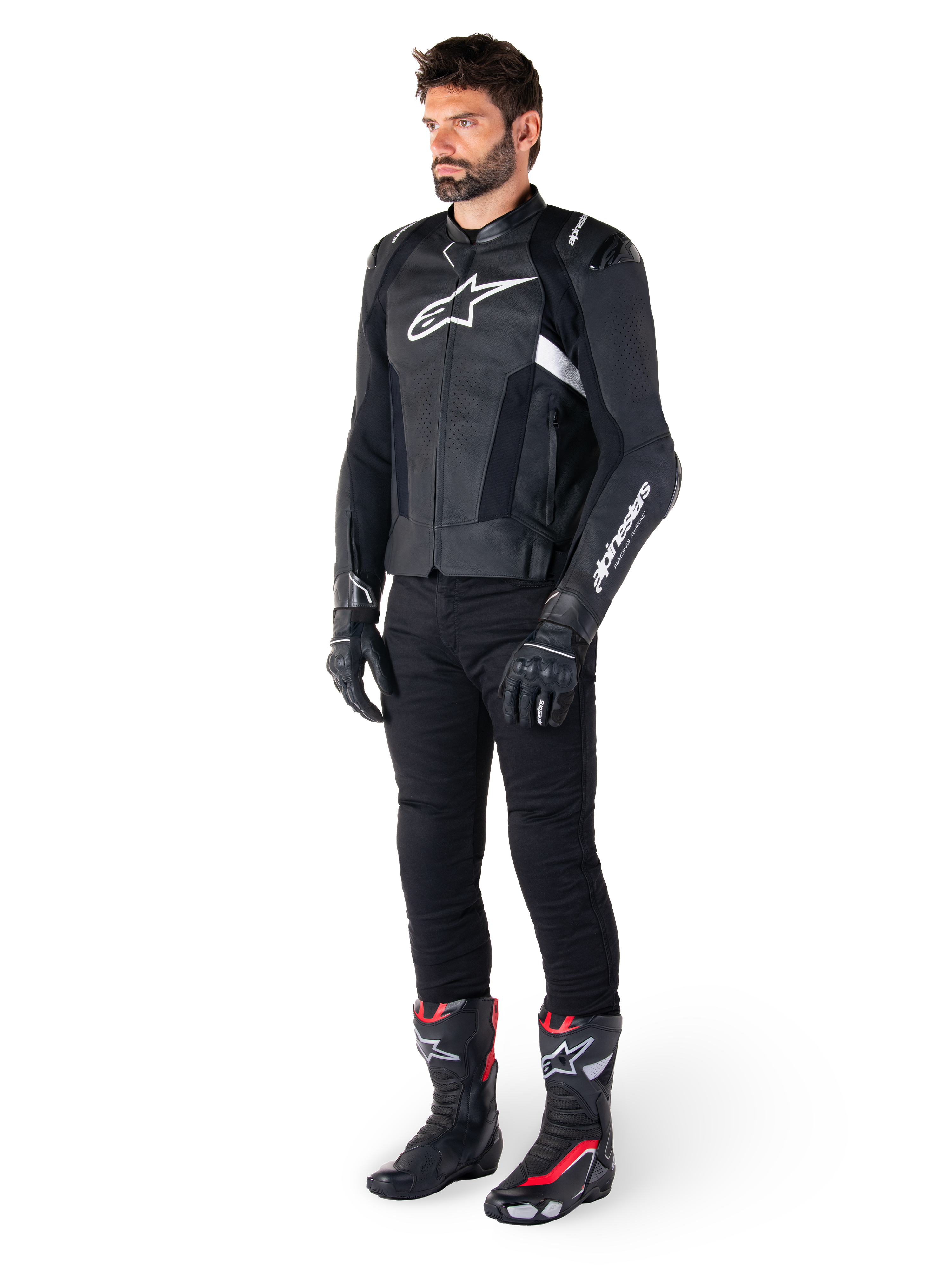 Mannelijke motorrijder die de Alpinestars Missile V3 lederen jas in het zwart en wit draagt, voorzien van een wit logo op de borst en geperforeerde lederen panelen, gecombineerd met een zwarte motorbroek, zwarte handschoenen en zwart-rode racelaarzen voor een complete sportieve motoroutfit.