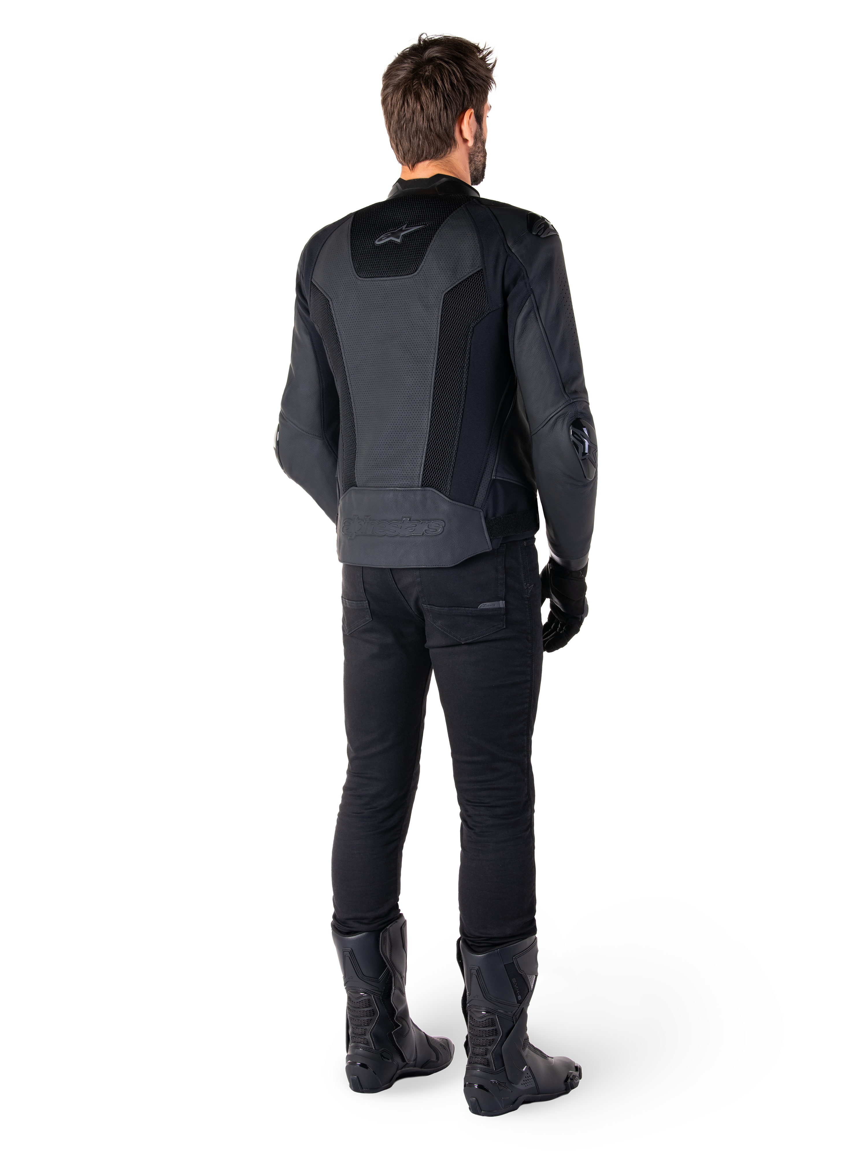 Achteraanzicht van een man die de Alpinestars Missile V3 Airflow leren jas in het zwart draagt, voorzien van uitgebreide geperforeerde panelen voor ventilatie, gecombineerd met een zwarte motorbroek en laarzen, met een gestroomlijnde race-esthetiek.