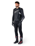 Alpinestars Missile V3 Airflow Leren Jas, zwart en wit, gedragen door een mannelijk model met zwarte motorbroek, zwarte handschoenen en racelaarzen met rode en witte accenten, voorzien van geperforeerd leer en witte logo's, performance motorrace-uitrusting