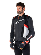 Alpinestars Missile V3 Airflow leren jas, zwart, wit en fluo rood, racing sport motorjas, gedragen door een model met bijpassende handschoenen, voorzien van geperforeerde leren panelen, een groot wit logo op de borst en zwarte schoudersliders.