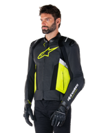 Mannelijk model draagt Alpinestars Missile V3 Airflow leren jas, zwart met Yellow Fluo en witte accenten, voorzien van geperforeerd leer voor maximale ventilatie, opvallend geel logo op de borst, gecombineerd met zwarte handschoenen en broek, sportieve motoruitrusting