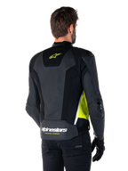 Alpinestars Missile V3 Airflow Leren Jas, achteraanzicht op een mannelijk model, zwart met fluo gele en witte accenten, voorzien van uitgebreide geperforeerde leren en mesh panelen op de rug, met een geel sterlogo en witte 'RACING AHEAD' tekst, gecombineerd met zwarte handschoenen en broek.