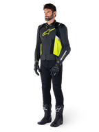 Mannelijk model in de Alpinestars Missile V3 Airflow leren jas, uitgevoerd in zwart, geel fluo en wit, gecombineerd met zwarte motorhandschoenen, broek en laarzen, toont het geperforeerde leren ontwerp en de racing-geïnspireerde esthetiek.