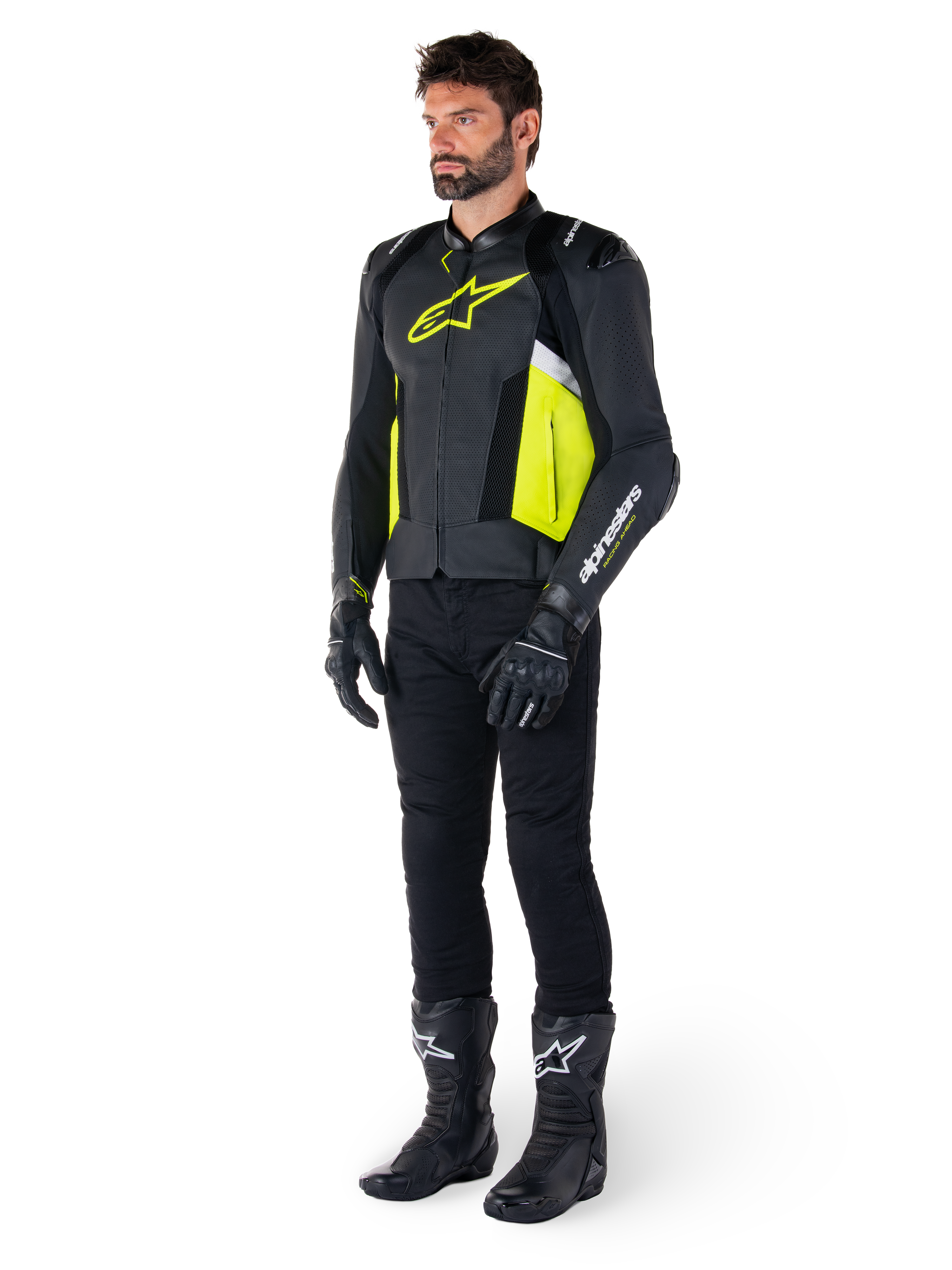 Mannelijk model in de Alpinestars Missile V3 Airflow leren jas, uitgevoerd in zwart, geel fluo en wit, gecombineerd met zwarte motorhandschoenen, broek en laarzen, toont het geperforeerde leren ontwerp en de racing-geïnspireerde esthetiek.