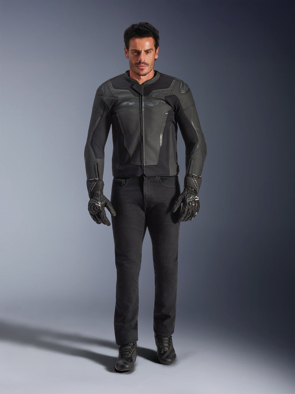 Alpinestars GP Force V2 leren jas in het zwart, gedragen door een mannelijke rijder met zwarte motorbroek, handschoenen en laarzen, slanke leren constructie in sportstijl met schoudersliders en geïntegreerde bescherming.