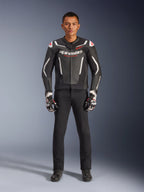 Mannelijk model draagt de Alpinestars GP Force V2 leren jas in zwart en wit, gecombineerd met een zwarte motorbroek en zwart-witte handschoenen, voorzien van opvallende Alpinestars-branding en rode schouderaccenten, professionele sportieve motoruitrusting