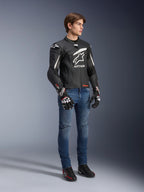 Alpinestars GP Plus R V4 Rideknit Leren Jas, motorleren jas, zwart en wit, gedragen door een model met blauwe jeans en zwarte handschoenen, met een opvallend wit Astars-logo op de borst, geperforeerde panelen en witte accenten op de schouders.