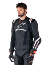 Male model wearing the Alpinestars Missile V3 Ignition Leather Jacket, Black with White and Orange accents, featuring prominent white logos, perforated leather sections, and protective shoulder armor, styled with racing gloves for a sport-racing look.
