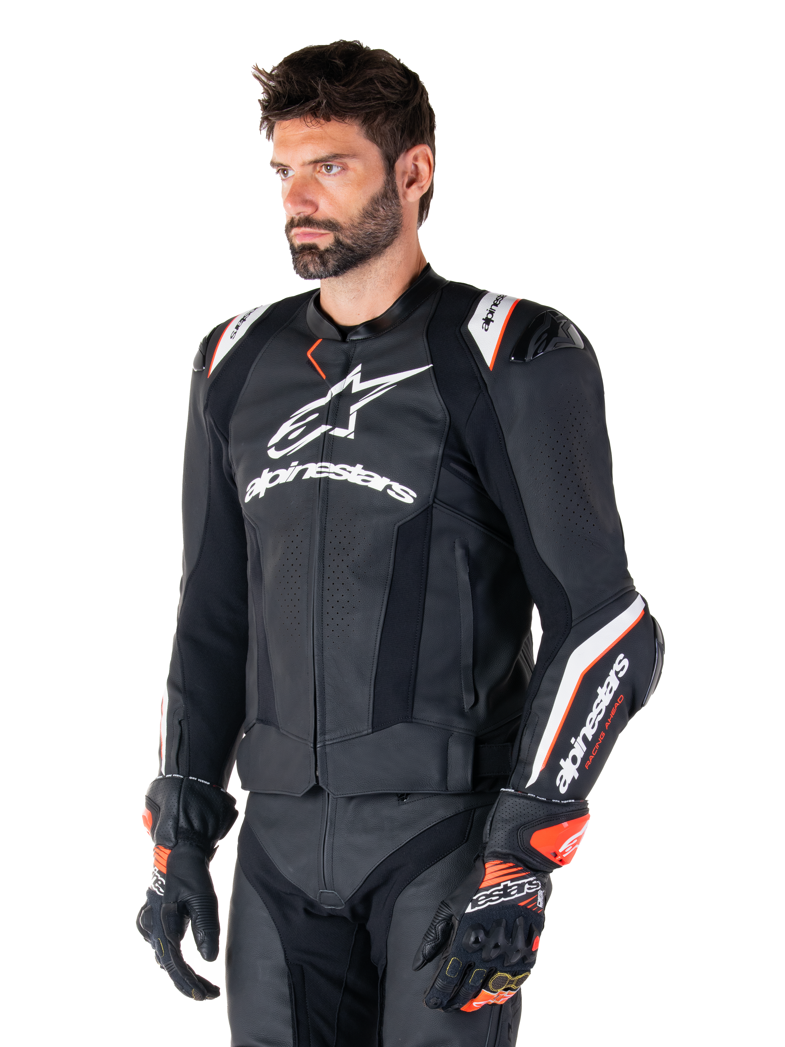 Mannelijk model in de Alpinestars Missile V3 Ignition leren jas, zwart met witte en oranje accenten, voorzien van opvallende witte logo's, geperforeerde leren delen en beschermende schouderprotectie, gestyled met racehandschoenen voor een sportieve race-look.