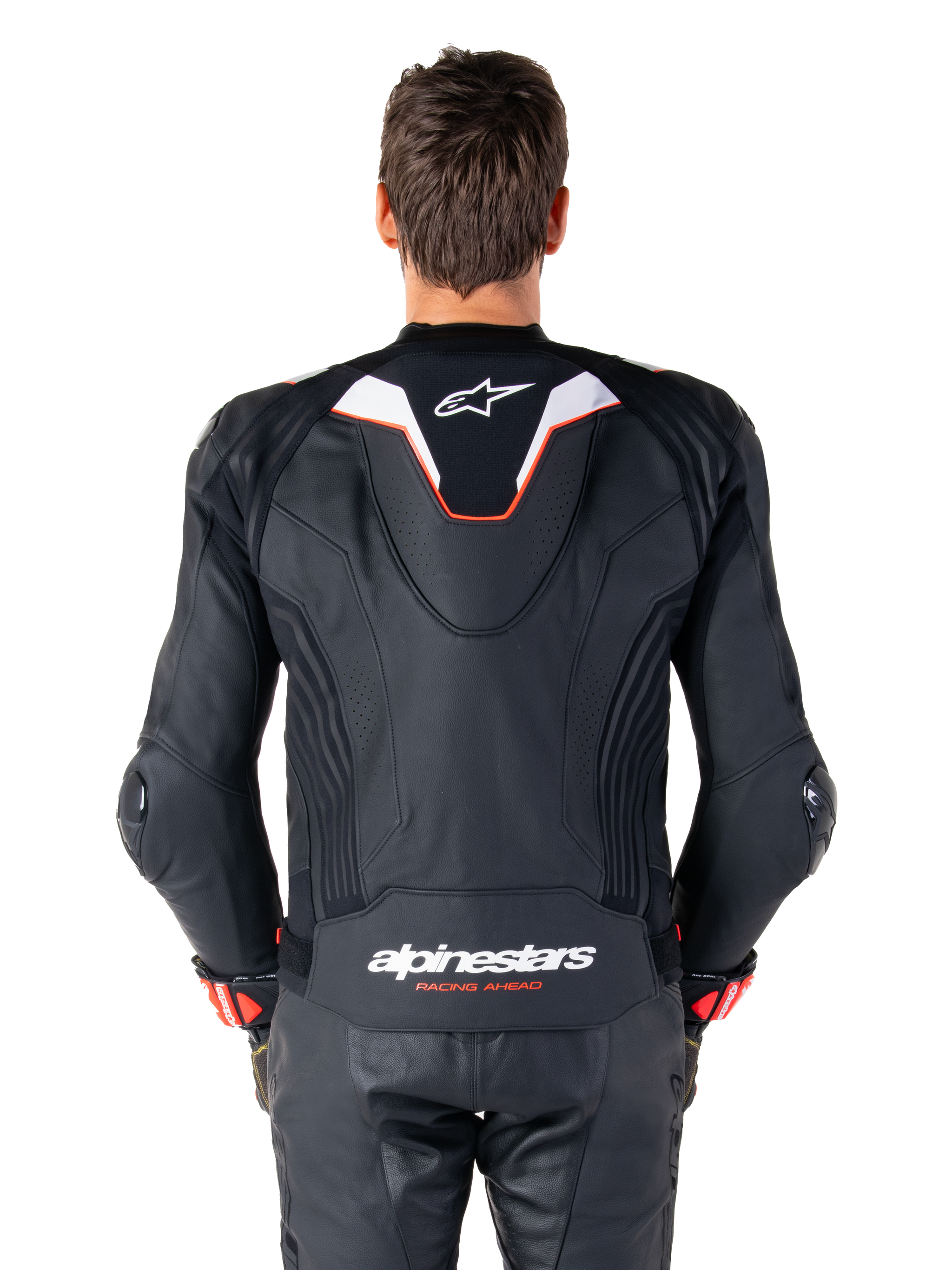 Rear view of a rider wearing the Alpinestars Missile V3 Ignition Leather Jacket, black leather with white and red accents, featuring a slim sport aero-hump with a white logo and 'alpinestars RACING AHEAD' branding on the lower back, paired with matching black leather racing pants and gloves.