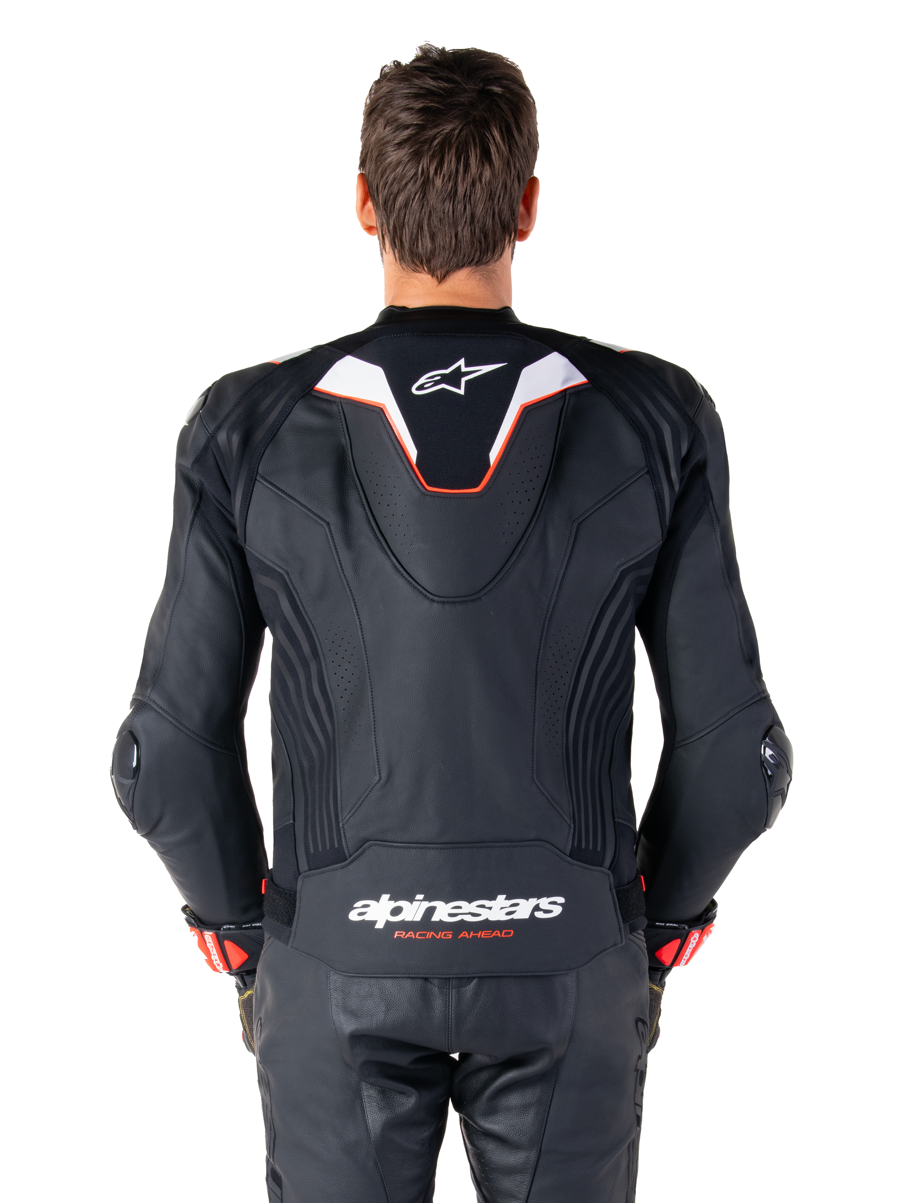 Alpinestars Missile V3 Ignition leren jas, achteraanzicht van een motorrijder, zwart leer met witte en rode accenten, voorzien van een slanke sport aero-hump met wit logo en 'alpinestars RACING AHEAD' branding op de onderrug, gecombineerd met bijpassende zwarte leren racebroek en handschoenen.