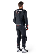Achteraanzicht van een motorrijder die de Alpinestars Missile V3 Ignition Leren Jas in het zwart draagt, met een slanke sport Aero-hump met witte en rode accenten, Alpinestars-logo op de onderrug, gecombineerd met bijpassende zwarte leren broek en zwart-witte racelaarzen, professionele sportieve rij-outfit