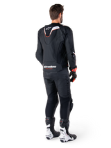 Rear view of a rider wearing the Alpinestars Missile V3 Ignition Leather Jacket in Black, featuring a slim sport Aero-hump with white and red accents, Alpinestars branding on the lower back, paired with matching black leather pants and black and white racing boots, professional sport riding outfit
