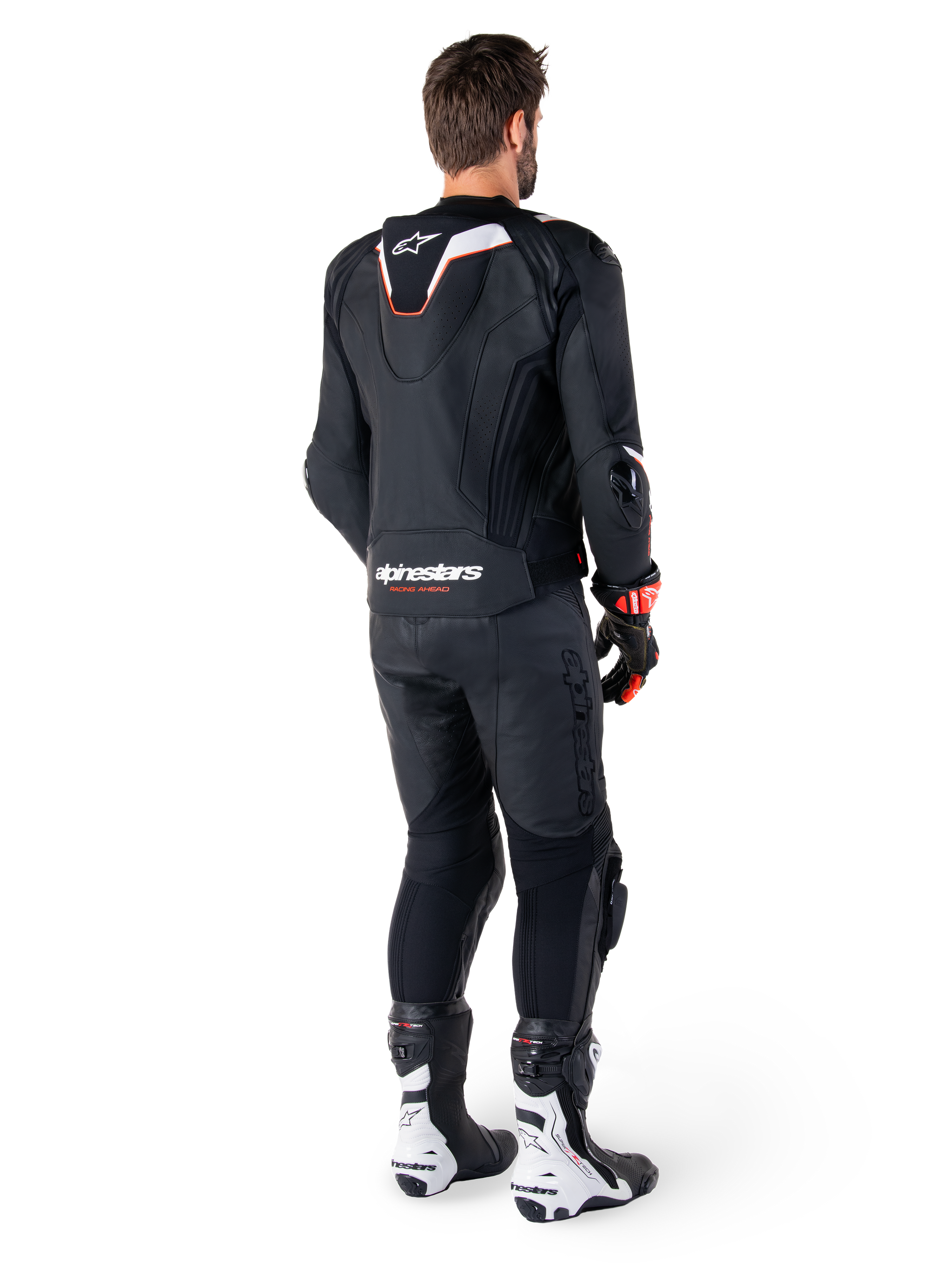 Rear view of a rider wearing the Alpinestars Missile V3 Ignition Leather Jacket in Black, featuring a slim sport Aero-hump with white and red accents, Alpinestars branding on the lower back, paired with matching black leather pants and black and white racing boots, professional sport riding outfit