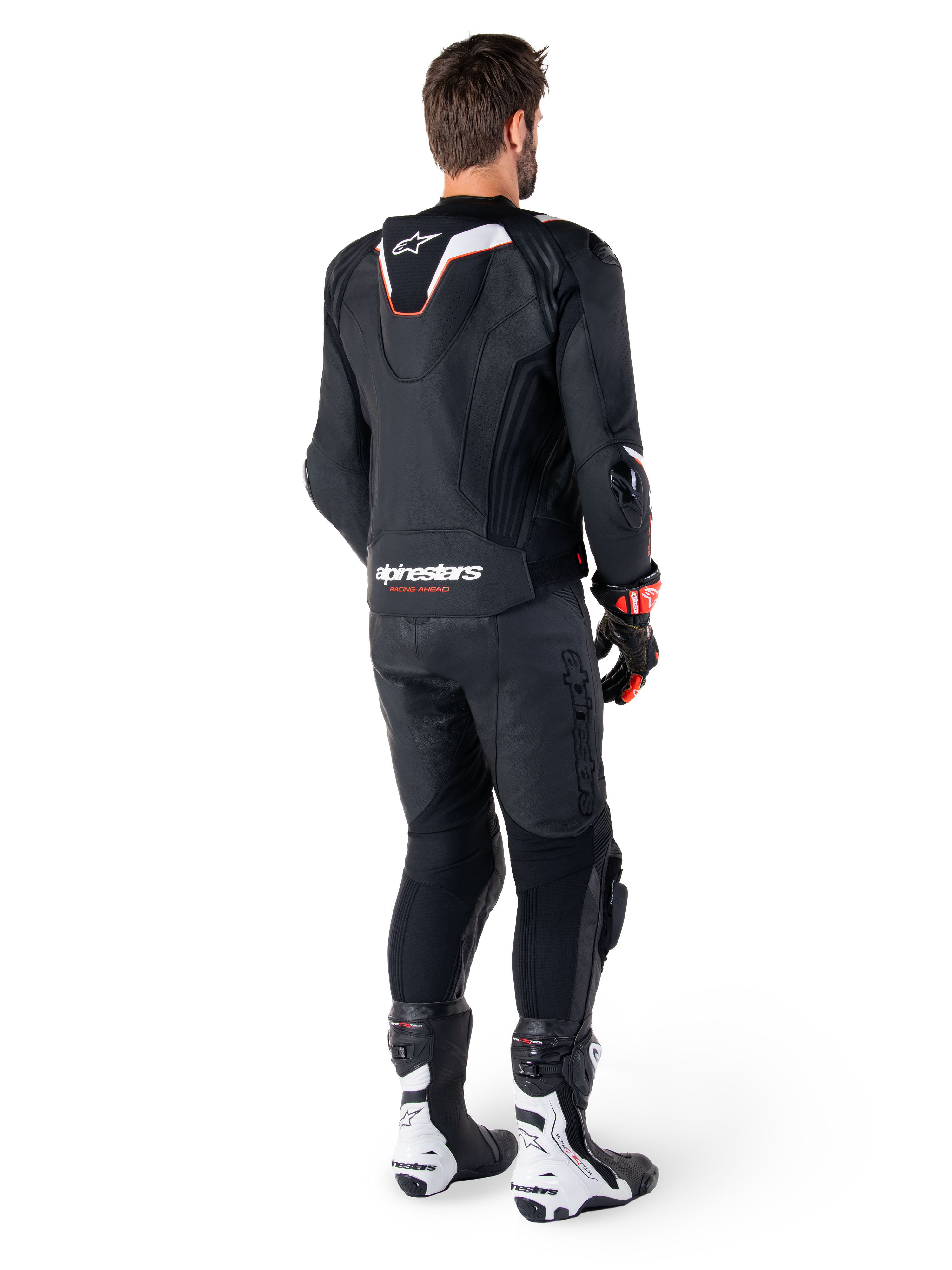 Achteraanzicht van een motorrijder die de Alpinestars Missile V3 Ignition Leren Jas in het zwart draagt, met een slanke sport Aero-hump met witte en rode accenten, Alpinestars-logo op de onderrug, gecombineerd met bijpassende zwarte leren broek en zwart-witte racelaarzen, professionele sportieve rij-outfit