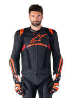 Alpinestars Missile V3 Ignition leren motorjas, racejas, zwart en rood fluo, gedragen met bijpassende racehandschoenen en leren broek, voorzien van geperforeerde ventilatie en opvallende Alpinestars branding, professionele race-uitrusting
