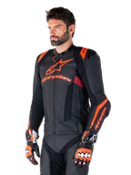 Alpinestars Missile V3 Ignition Leren Jas, zwart met fluo rood en donkerrode accenten, gedragen door een mannelijk model met bijpassende racehandschoenen en leren broek, opvallende Alpinestars-branding, geperforeerde leren panelen en externe schouderprotectoren, professionele motorrace-uitrusting