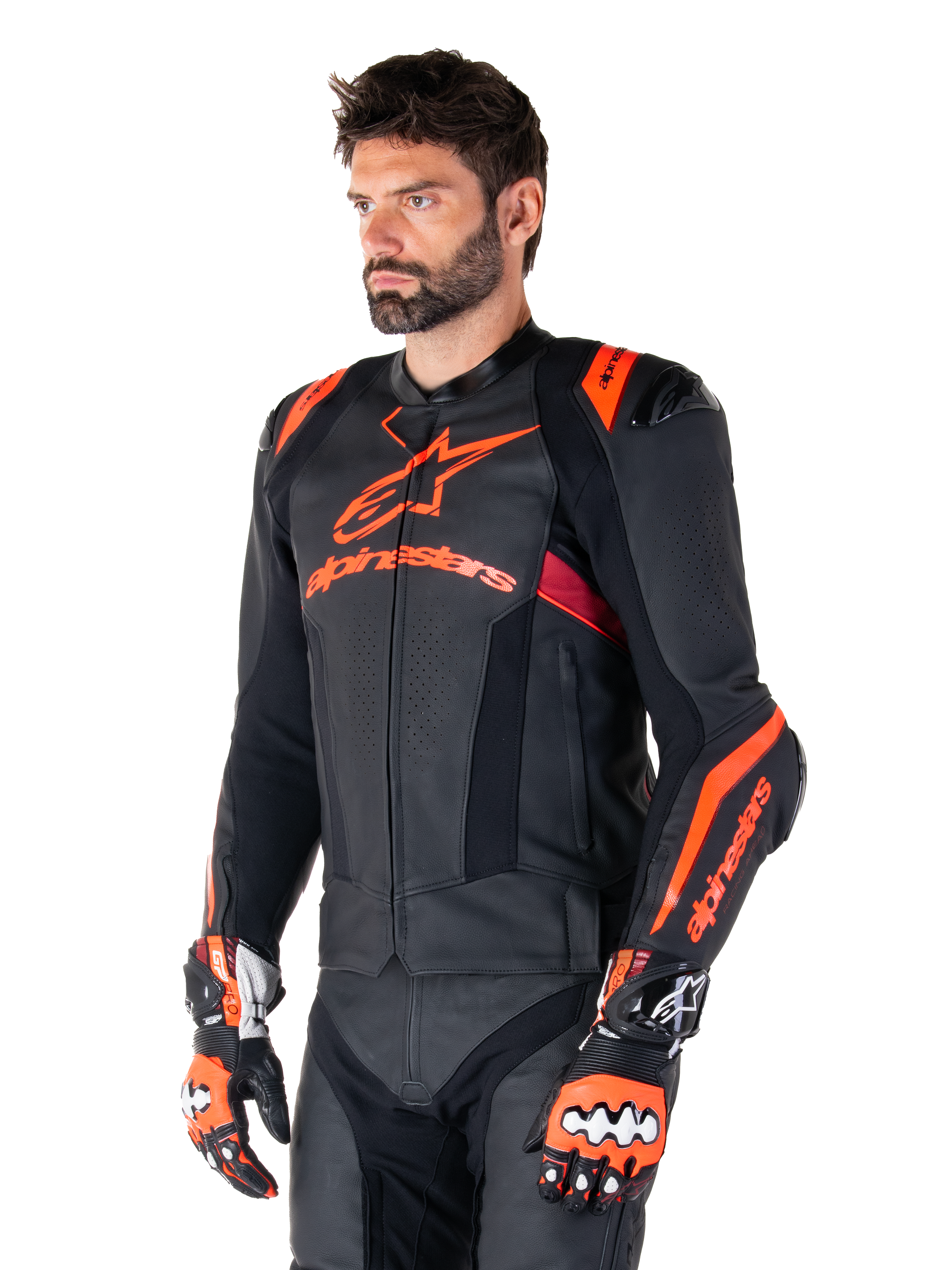 Alpinestars Missile V3 Ignition Leren Jas, zwart met fluo rood en donkerrode accenten, gedragen door een mannelijk model met bijpassende racehandschoenen en leren broek, opvallende Alpinestars-branding, geperforeerde leren panelen en externe schouderprotectoren, professionele motorrace-uitrusting
