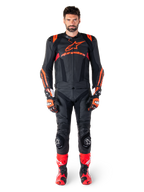 Mannelijk model draagt Alpinestars Missile V3 Ignition leren jas in Black Red Fluo Dark Red, complete motorrace-uitrusting inclusief bijpassende leren broek, racehandschoenen en laarzen, voorzien van opvallende Alpinestars-branding op de borst, naar voren gerichte pose, professionele sport-rijoutfit