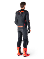 Alpinestars Missile V3 Ignition leren jas, race-sportmotorjas, zwart en fluo rood, achteraanzicht van een rijder die een volledige race-outfit draagt met bijpassende leren broek, handschoenen en rode laarzen, voorzien van een sport Aero-hump en opvallende merknaam op de onderrug.