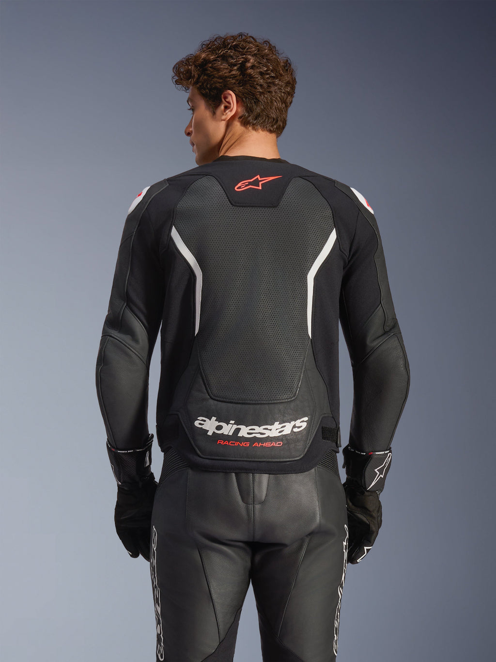 Alpinestars GP Force V2 Air Leren Jas, zwart met witte en rode accenten, achteraanzicht met geperforeerd leren rugpaneel, witte Alpinestars-branding en rode logo-details, gedragen met bijpassende zwarte leren racebroek en handschoenen.