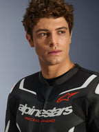 Portret van een mannelijk model dat de Alpinestars GP Force V2 Air leren jas in zwart en wit draagt, met geperforeerde leren constructie, opvallend wit logo en rode 'RACING AHEAD' tekst op de borst, sportieve motorrijuitrusting