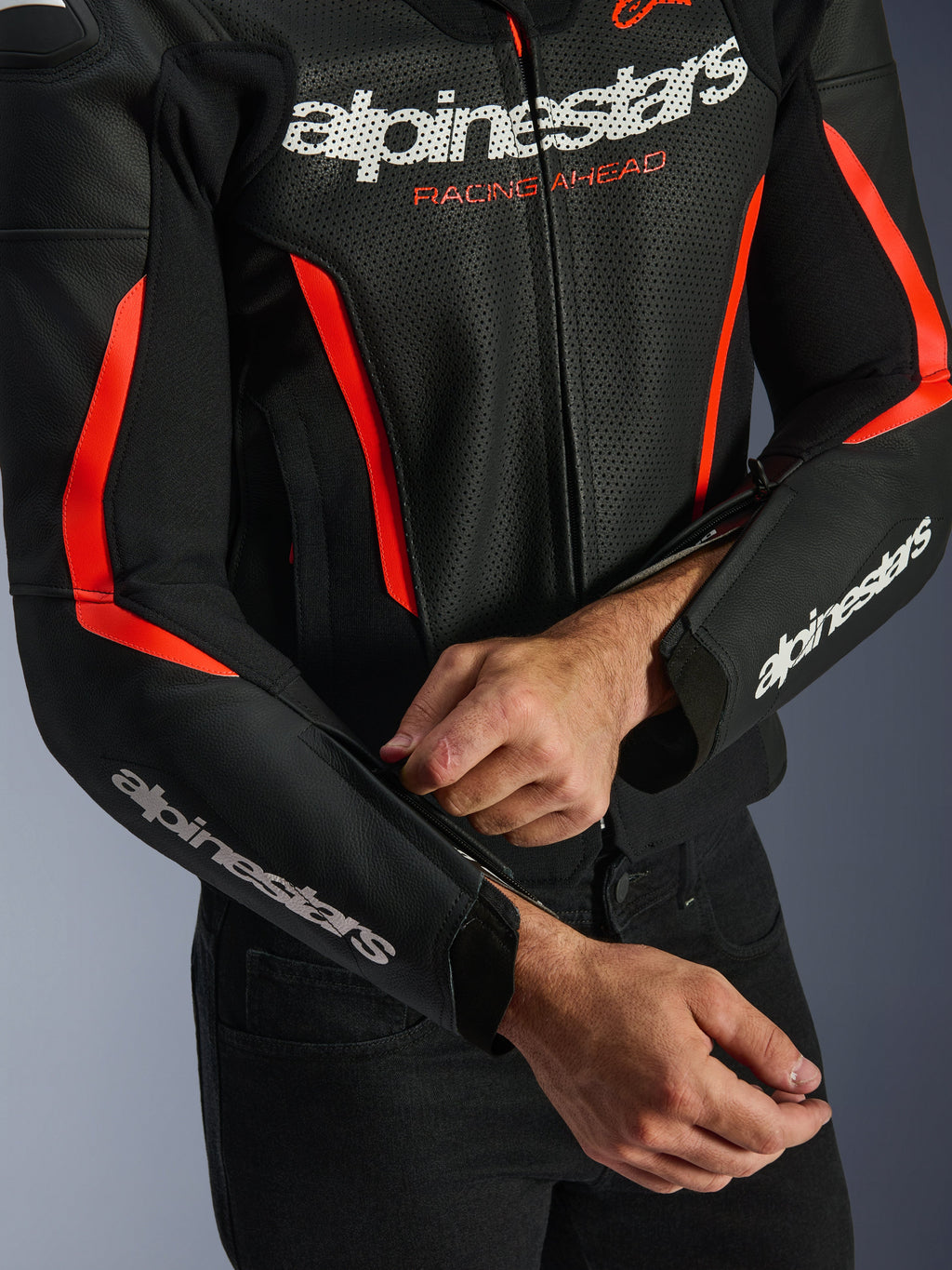 Alpinestars GP Force V2 Air Leather Jacket in Black and Red Fluo, close-up showing perforated leather construction, white branding on chest and sleeves, and a rider adjusting the forearm zipper for a tailored fit.