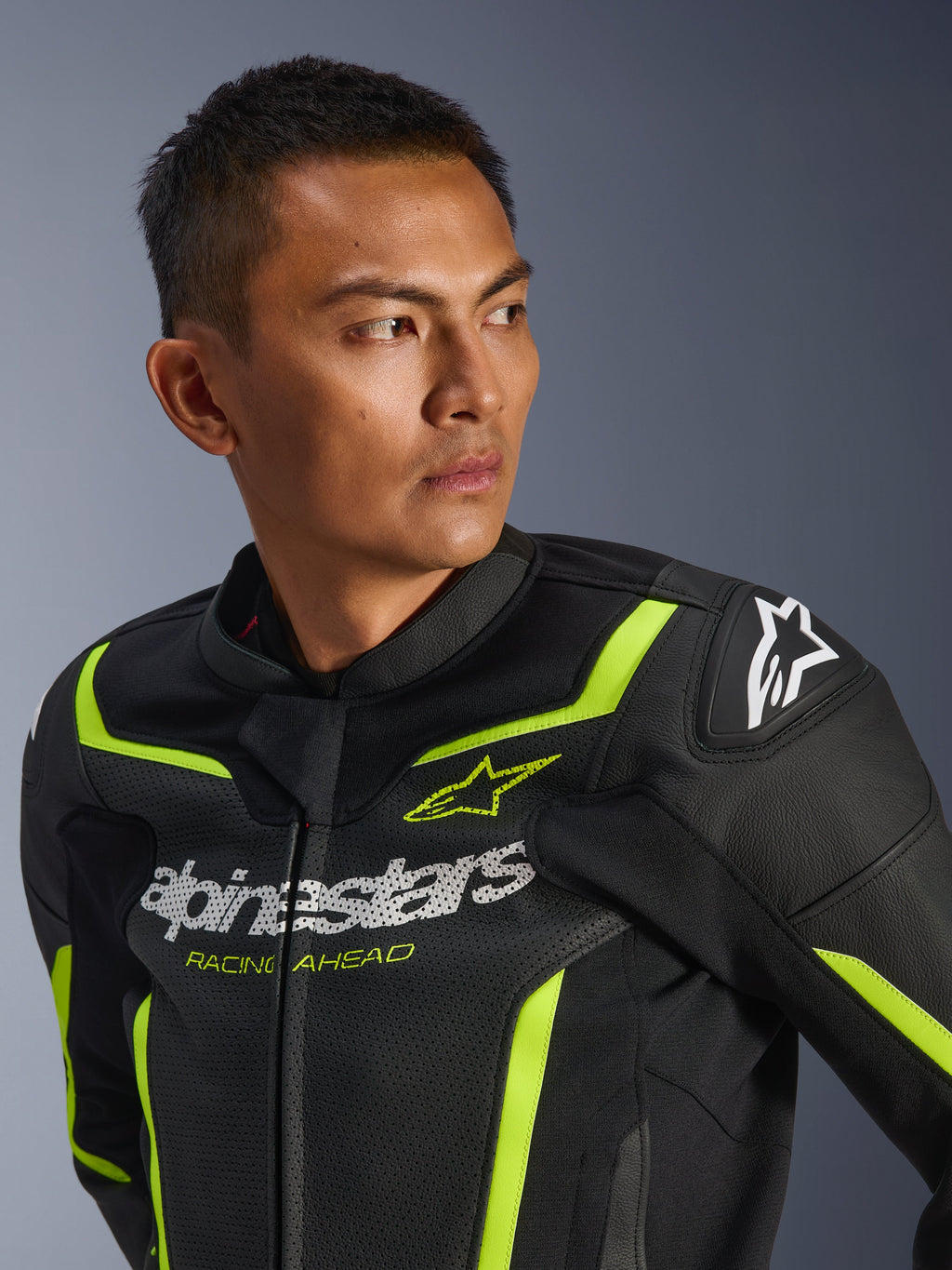 Alpinestars GP Force V2 Air Leren Jas, zwart en geel fluo, geperforeerde sportmotorjas met wit logo op de borst en de tekst 'Racing Ahead', neon accenten en beschermende schoudersliders, gedragen door een mannelijk model.