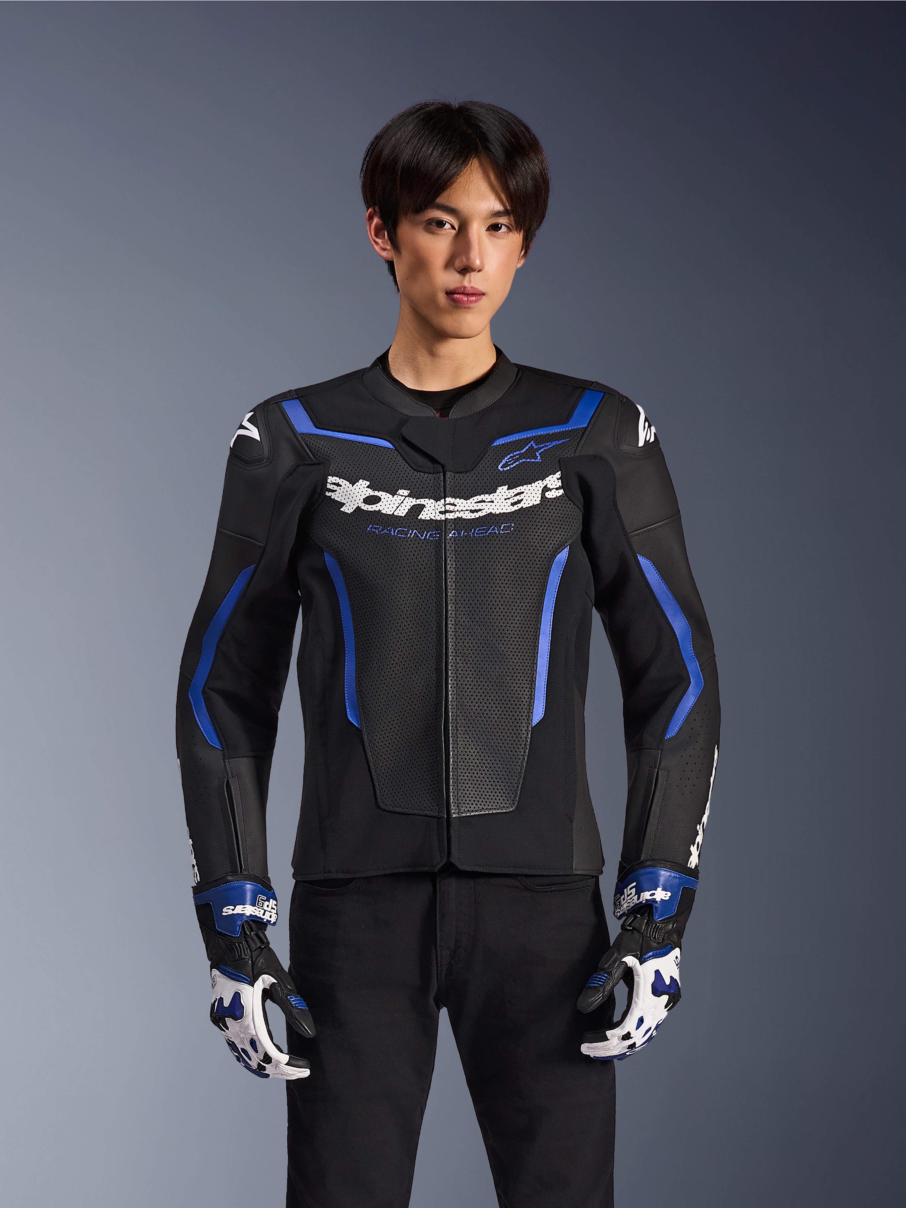 Alpinestars GP Force V2 Airflow Leather Jacket, motorjas van geperforeerd leer, zwart met metallic blauwe accenten, gedragen door een model met bijpassende racehandschoenen en zwarte broek, professionele sportieve motoruitrusting
