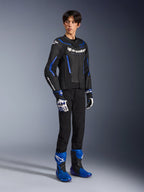 Male rider wearing the GP Force V2 Airflow Leather Jacket in Black Metallic Blue, paired with matching racing gloves and blue boots, featuring perforated leather and bold Alpinestars branding, professional motorcycle road gear.