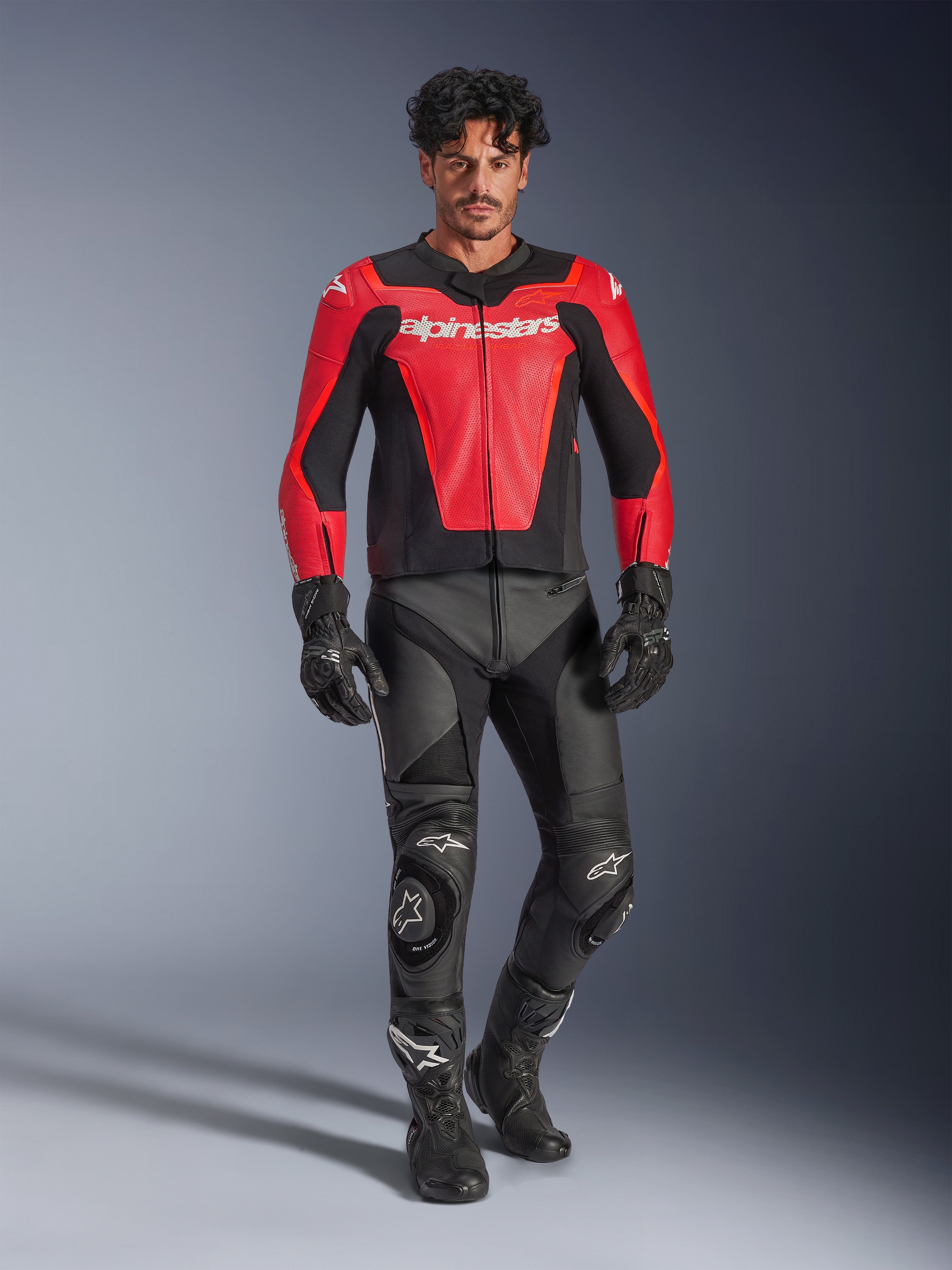 Alpinestars GP Force V2 Air Leren Jas, rood en zwart, geperforeerd leer met witte branding, gedragen door een model met zwarte leren racebroek en handschoenen, professionele motoruitrusting
