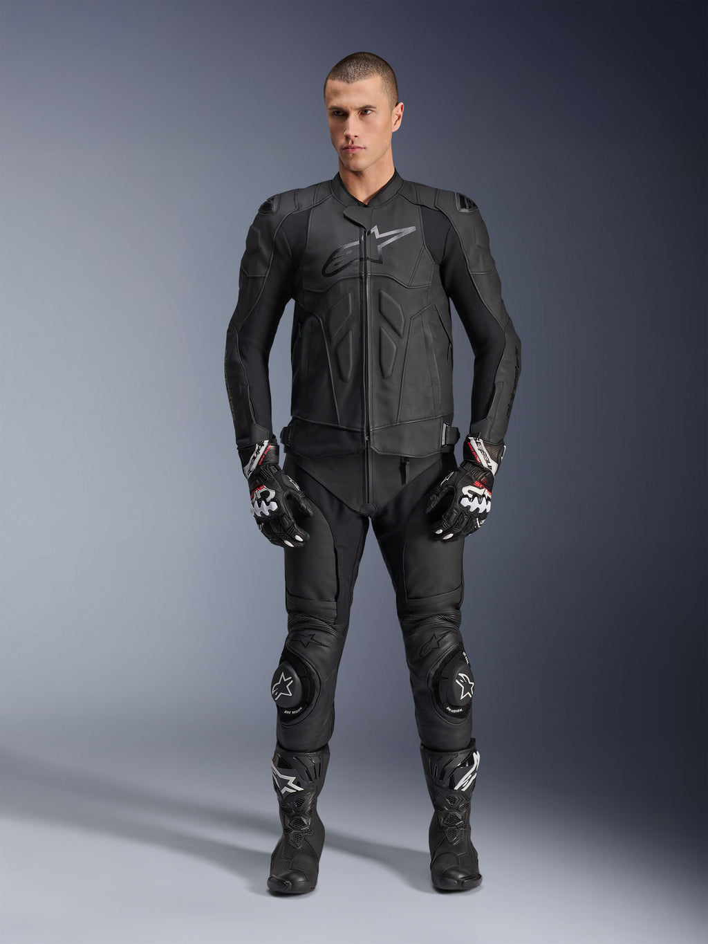 Alpinestars Dusk Leren Jas, zwart, gedragen door een mannelijk model als onderdeel van een complete race-geïnspireerde outfit met bijpassende leren broek, handschoenen en laarzen, strak ergonomisch ontwerp met bescherming op de schouders en logo op de borst