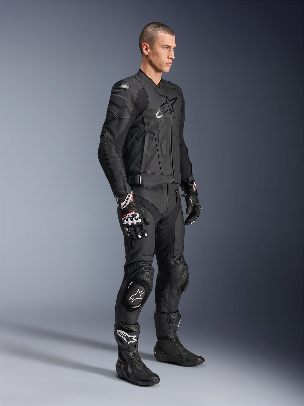Alpinestars Dusk leren jas, zwart, gedragen door een mannelijk model met bijpassende leren motorbroek, racehandschoenen en laarzen, voorzien van een opvallend sterlogo op de borst en een ergonomisch sportief ontwerp voor op de weg