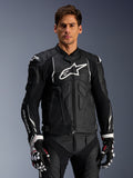 Alpinestars Dusk Leather Jacket, zwart en wit, leren motorjas met gewatteerde beschermingszones en witte logo's, gedragen met zwart-witte racehandschoenen met rode accenten, professionele sportieve motoruitrusting