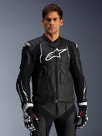 Alpinestars Dusk Leather Jacket, zwart en wit, leren motorjas met gewatteerde beschermingszones en witte logo's, gedragen met zwart-witte racehandschoenen met rode accenten, professionele sportieve motoruitrusting
