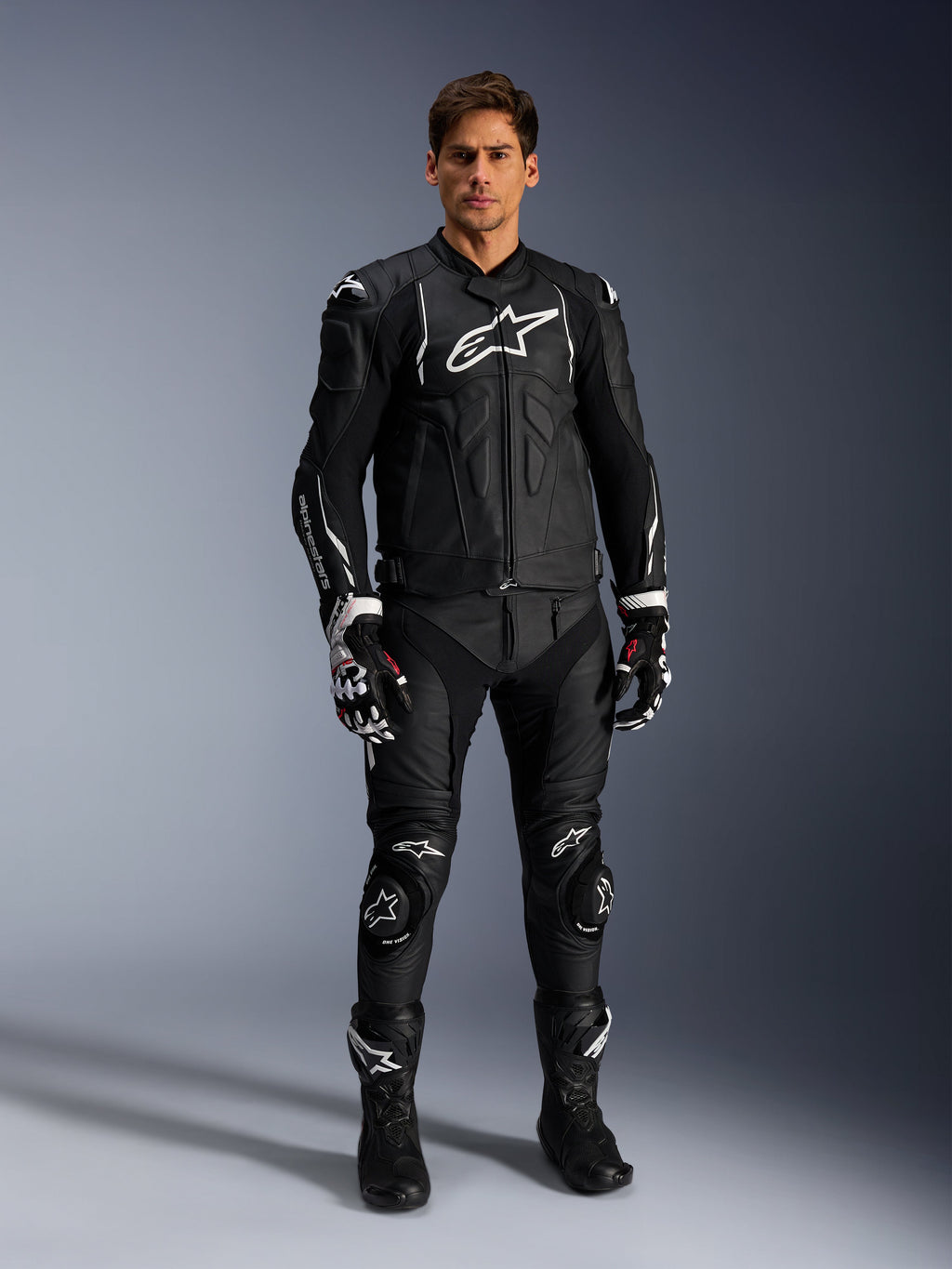 Alpinestars Missile V3 Leren Broek, zwart, gedragen door een mannelijke rijder als onderdeel van een volledige leren motorrace-outfit, voorzien van witte Alpinestars-branding, beschermende kniesliders, racelaarzen en handschoenen.