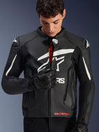 Alpinestars GP Plus V4 Leren Jas, zwart en wit, mannelijk model rits de voorzijde dicht waarbij de rode merkdetails aan de binnenkant zichtbaar zijn, voorzien van opvallende witte Alpinestars-logo's op de borst en schouders, gedragen met zwarte leren motorhandschoenen, sportieve leren motorkleding