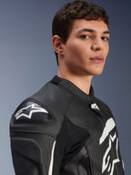 Alpinestars GP Plus V4 leren jas, zwart en wit, gedragen door een mannelijk model, met een wit Alpinestars-logo en DFS-schouderglijders, race-afgeleide lederen constructie voor sportief rijden