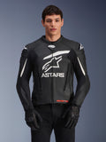 Alpinestars GP Plus V4 leren motorjas, zwart met witte accenten, groot wit ASTARS-logo en ster-grafiek op de borst, gedragen met zwarte motorhandschoenen en broek, strak race-afgeleid sportief leren ontwerp