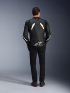 Alpinestars GP Plus V4 leren jas in zwart en wit, model van achteren gezien, gecombineerd met een zwarte broek en motorlaarzen, voorzien van witte panelen op de schouders en Alpinestars-logo's op de mouwen en onderrug.