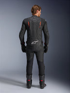 Alpinestars Dusk Airflow Leren Jas, zwart en fluorood, achteraanzicht met uitgebreide perforaties en groot wit logo op de onderrug, gedragen met bijpassende leren race-uitrusting inclusief broek, laarzen en handschoenen