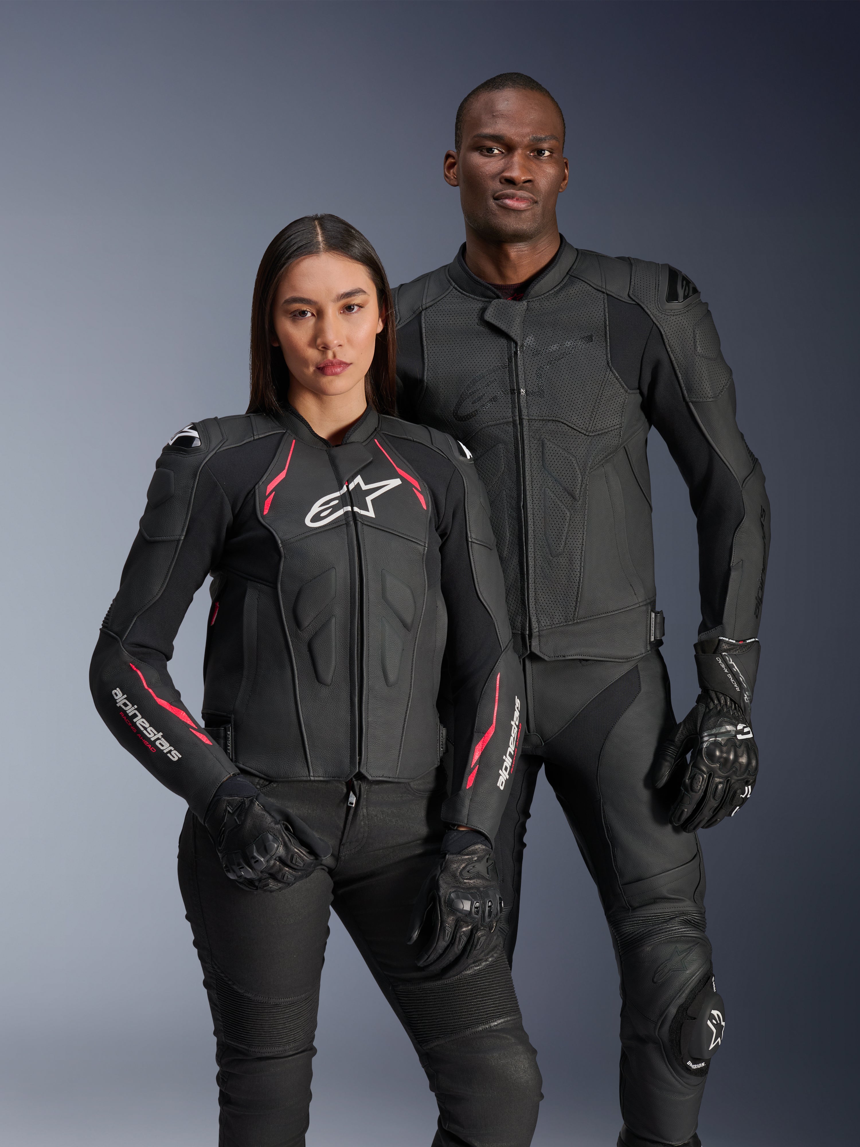 Alpinestars Dusk Airflow en Stella Dusk leren jassen, mannelijke en vrouwelijke motorrijders in zwarte leren motorjassen, herenjas met geperforeerd leer voor ventilatie, damesjas met rode accenten en witte logo's, gecombineerd met zwarte motorbroek en handschoenen, sportieve motorrijuitrusting