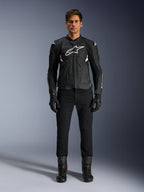 Alpinestars Dusk Airflow Leren Jas, zwart en wit, leren motorjas met geperforeerde panelen voor luchtstroom, wit Astars-logo op de borst, gedragen door een mannelijke rijder met zwarte broek, handschoenen en motorlaarzen, professionele studio-opname voor sportieve motoruitrusting.