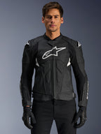 Alpinestars Dusk Airflow leren jas, zwart en wit, leren motorjas gedragen door een model, voorzien van geperforeerde leren panelen voor ventilatie, een groot wit logo op de borst en externe schouder sliders.