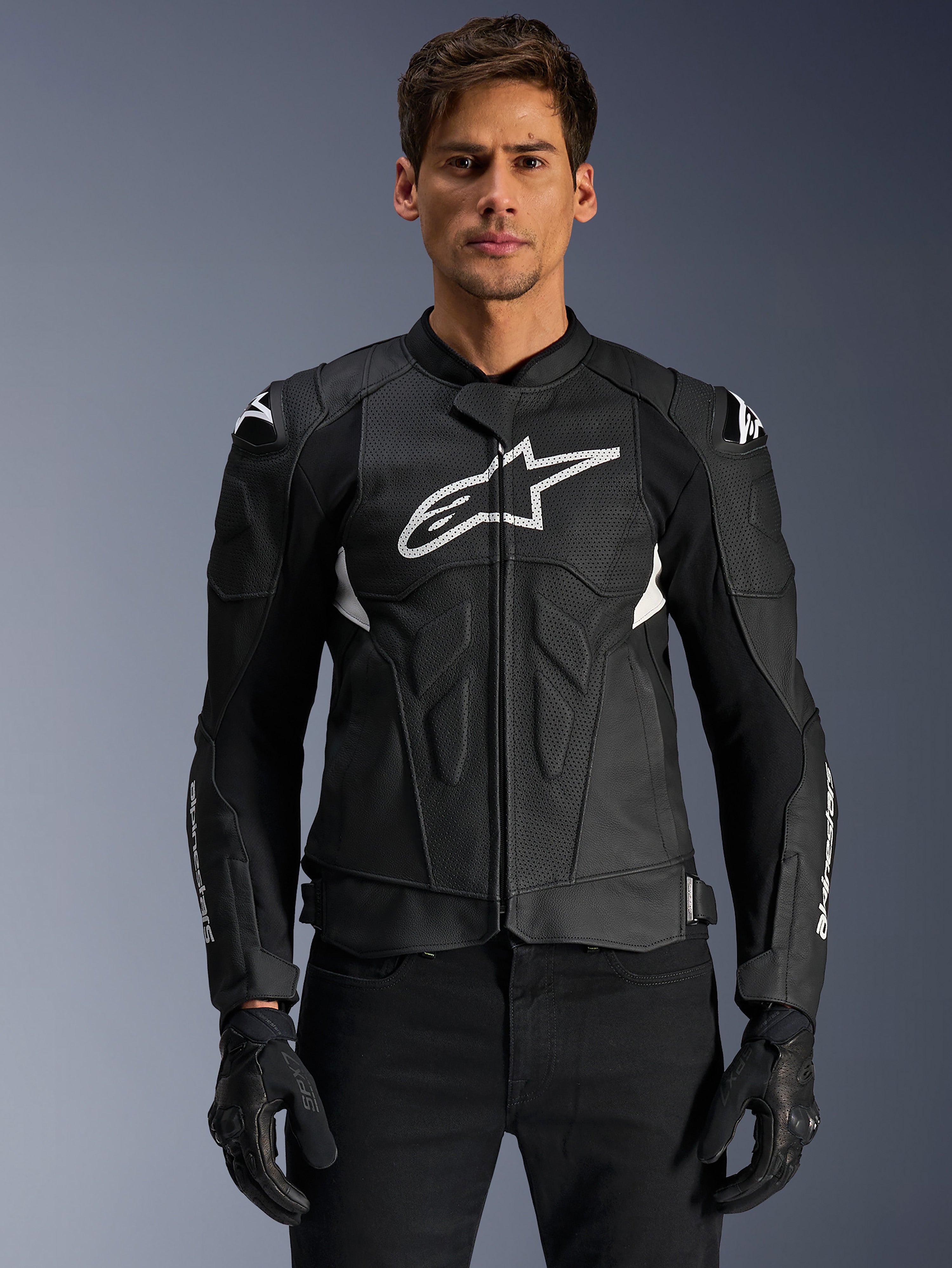 Alpinestars Dusk Airflow leren jas, zwart en wit, leren motorjas gedragen door een model, voorzien van geperforeerde leren panelen voor ventilatie, een groot wit logo op de borst en externe schouder sliders.